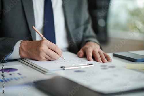 Hands of senior entrepreneur taking notes when analyzing data in reports