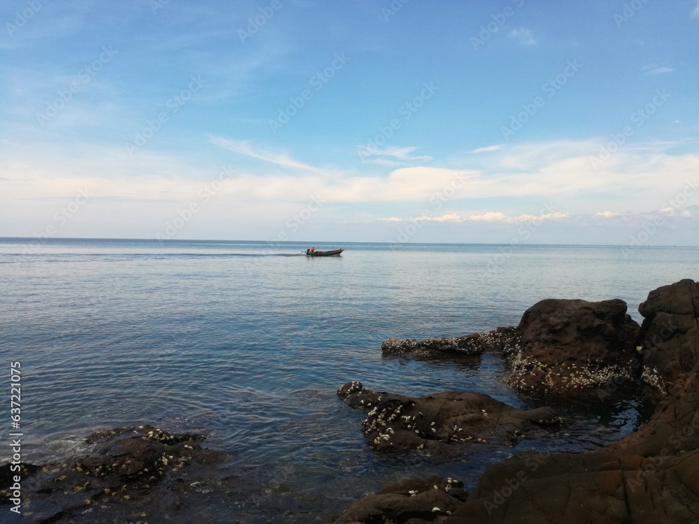 Seascape rocks on sea with boat and blue sky