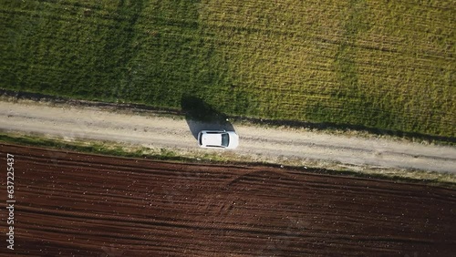 An aerial view of a landscape with distinct sections of green and brown fields, separated by a path where a white car is parked. The contrast between the cultivated land creates an interesting geometr