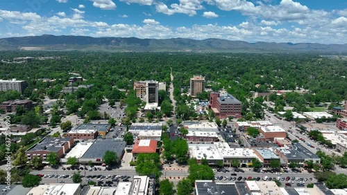 High descending shot of Fort Collins Colorado skyline. Beautiful summertime establishing shot. Green trees and mountain background on blue sky day.