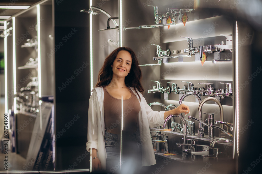 Young woman client choosing sanitary taps standing with catalog near the showcase of plumbing shop Young woman client choosing sanitary taps standing with catalog near the showcase of plumbing shop