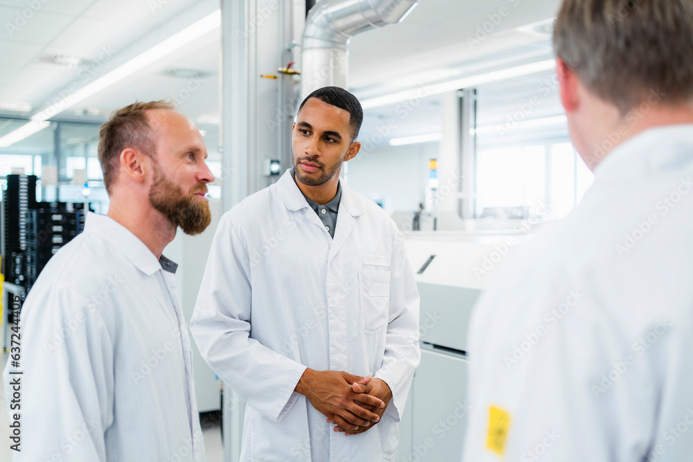 Team of competent electrical technicians in lab coats having meeting in electronics factory Team of competent electrical technicians in lab coats having meeting in electronics factory