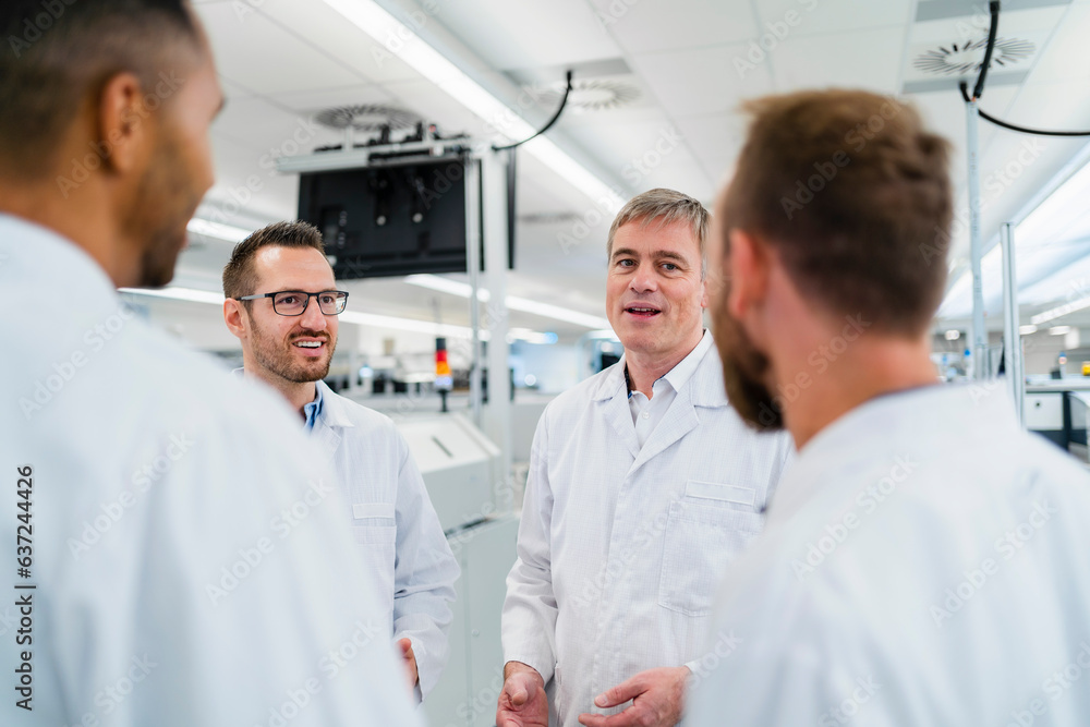 Team of competent electrical technicians in lab coats having meeting in electronics factory Team of competent electrical technicians in lab coats having meeting in electronics factory