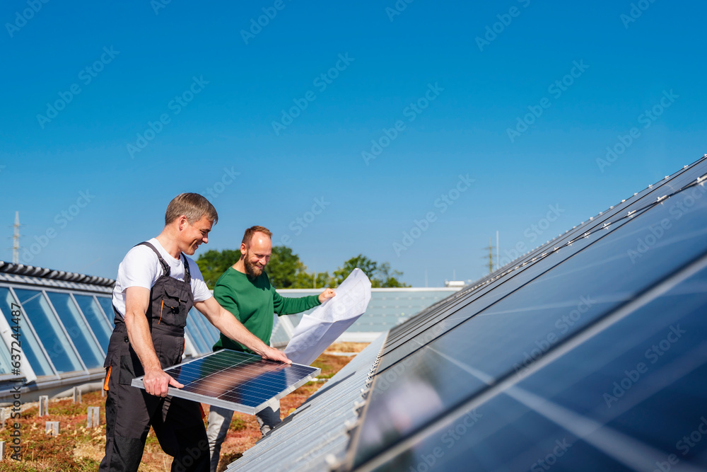 Craftsman installing solar panel on the roof of a company building with colleague holding plan Craftsman installing solar panel on the roof of a company building with colleague holding plan