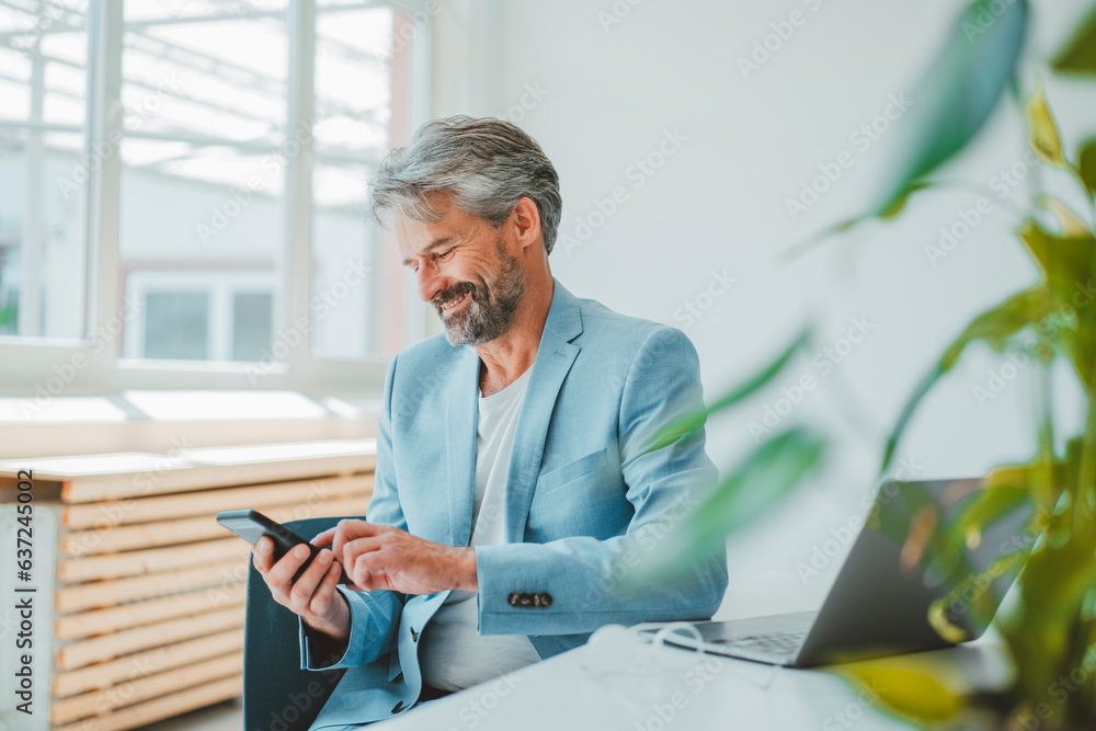 Smiling businessman using mobile phone sitting at desk in office Smiling businessman using mobile phone sitting at desk in office
