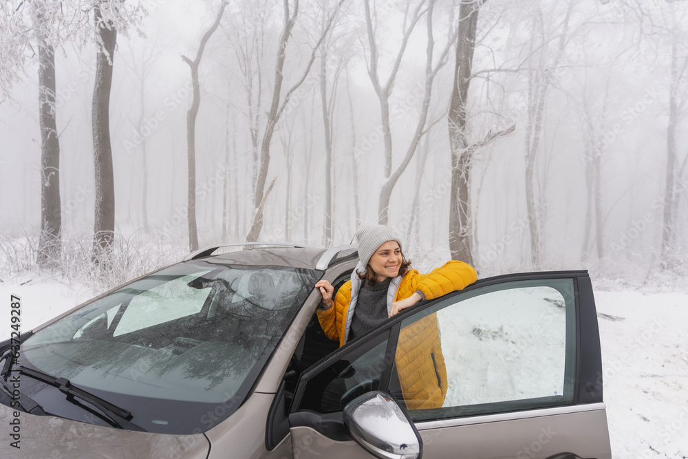 Young caucasian woman traveler driver standing next to her car in snowy forest
