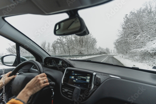 View from the car on the road in a snowy forest, with hands on the steering wheel. Slip road and driving safety concept