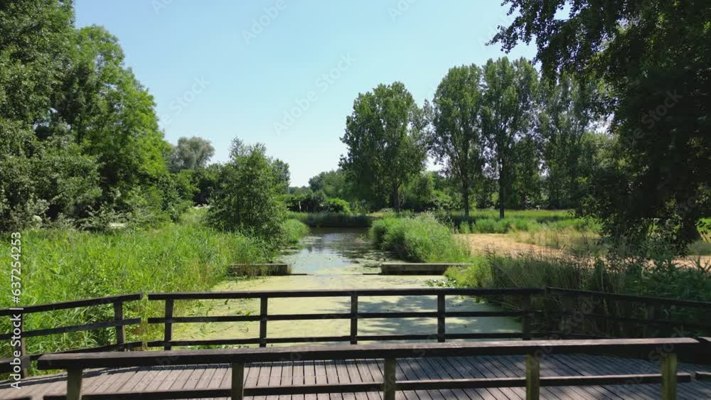 Drone shot over a footbridge over a canal in the nature park of Almere, Flevoland province, the Netherlands. Drone shot over a footbridge over a canal in the nature park of Almere, Flevoland province, the Netherlands.
