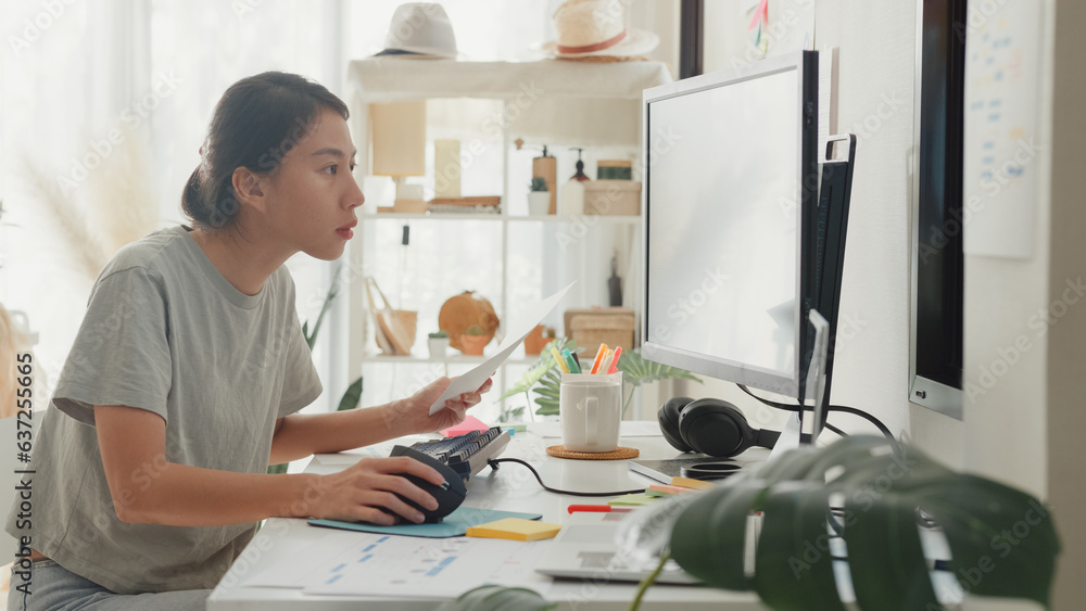 Fototapeta premium Side view of professional young Asia girl IT development programmer typing on keyboard coding programming fixing data code on computer screen and laptop on table in workroom at house office.