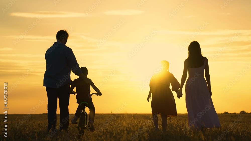 Dad, Mom teaches children to ride bike, sunset. Childhood dream of riding bike. Father teaches his child to keep balance while sitting on bicycle. Family life, mother, child, parental support. Kids