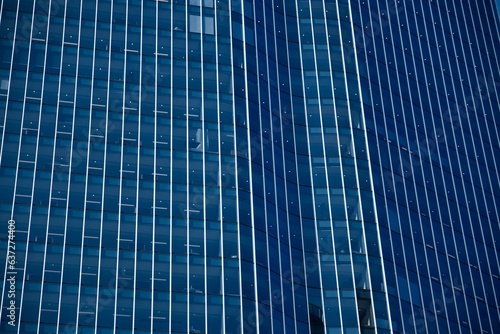 Abstract dark blue facade of an office building. Blue glass facade office building with straight white vertical lines. Modern-looking skyscraper with blue-colored glass windows. Modern city skyline. 