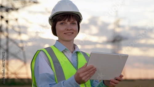Woman electrician with tablet at power distribution substation in evening