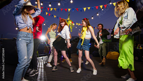 Young caucasian women dancing on a rooftop party. Fun time with friends enjoying rooftop party music, celebrating weekend reunion gathering.