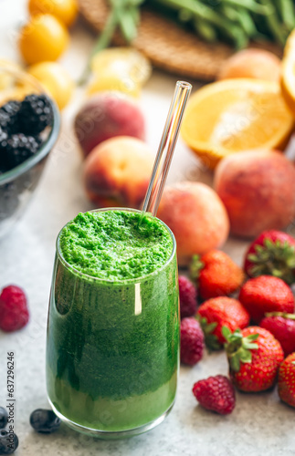 Glass of green smoothie on blurred kitchen table with berries.