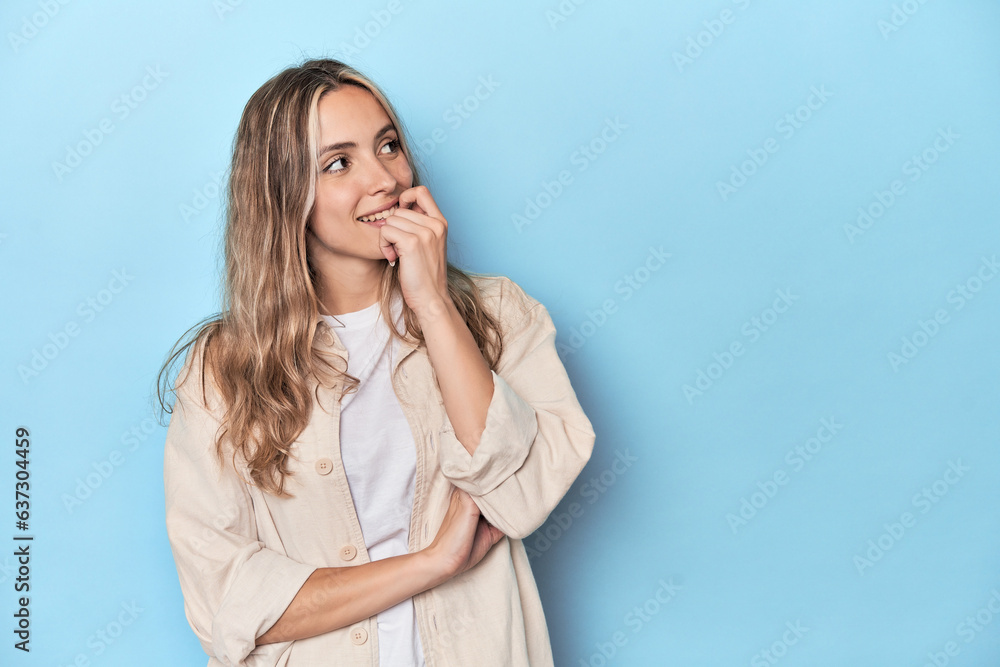 Blonde young caucasian woman in blue studio relaxed thinking about something looking at a copy space. Blonde young caucasian woman in blue studio relaxed thinking about something looking at a copy space.