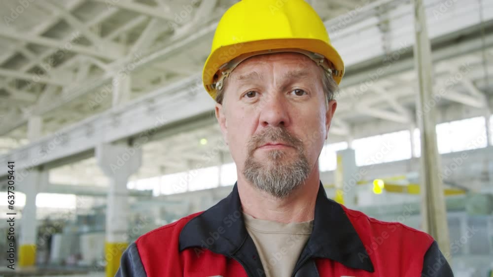 Portrait of mature male technician in hardhat and workwear standing in industrial plant and posing on camera with smile Portrait of mature male technician in hardhat and workwear standing in industrial plant and posing on camera with smile
