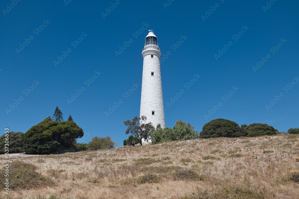 Beautiful old white lighthouse on Rottnest Island. Wadjemup Lighthouse at Rottnest Island, Western Australia. Tall white historic lighthouse on a hill in front of a perfect blue sky. 