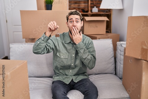 Hispanic man with beard holding keys of new home covering mouth with hand, shocked and afraid for mistake. surprised expression © Krakenimages.com