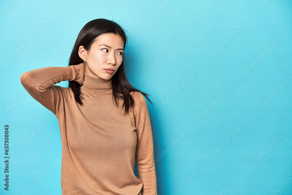 Young Asian woman in brown turtleneck, touching back of head, thinking and making a choice. Young Asian woman in brown turtleneck, touching back of head, thinking and making a choice.