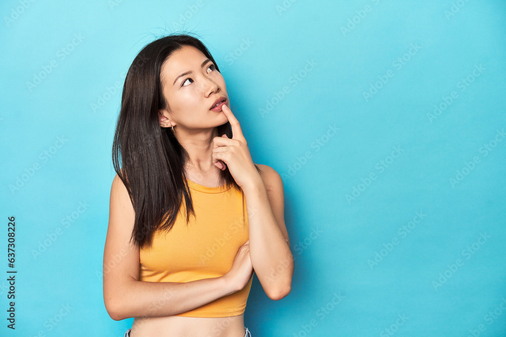Asian woman in summer yellow top, studio setup, looking sideways with doubtful and skeptical expression. Asian woman in summer yellow top, studio setup, looking sideways with doubtful and skeptical expression.