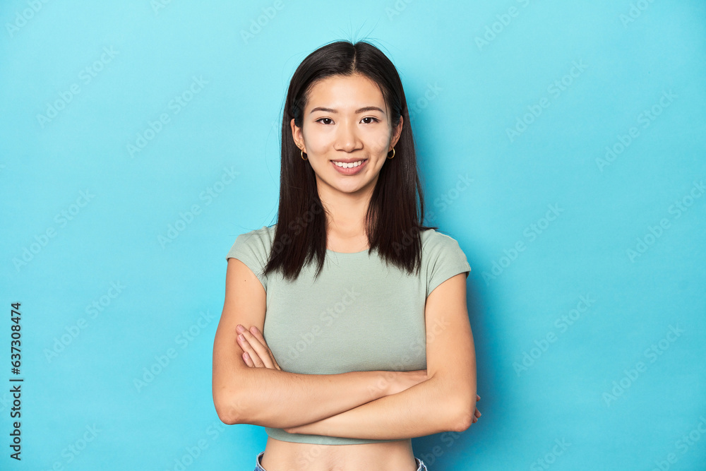 Asian woman in summer green top, studio backdrop, who feels confident, crossing arms with determination. Asian woman in summer green top, studio backdrop, who feels confident, crossing arms with determination.