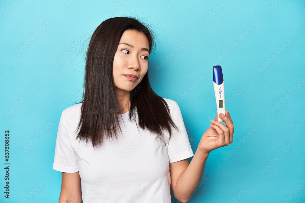 Young Asian woman holding a pregnancy test, studio shot. Young Asian woman holding a pregnancy test, studio shot.