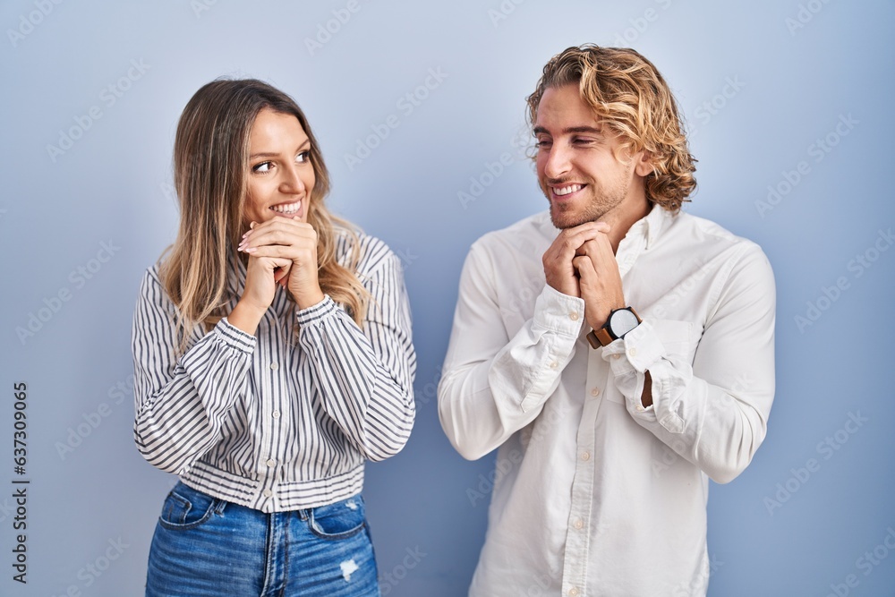 Young couple standing over blue background laughing nervous and excited with hands on chin looking to the side Young couple standing over blue background laughing nervous and excited with hands on chin looking to the side