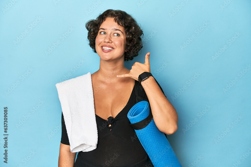 Athletic young woman with yoga mat showing a mobile phone call gesture with fingers.