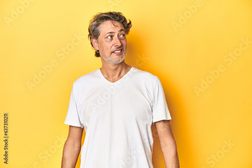 Middle-aged man posing on a yellow backdrop relaxed and happy laughing, neck stretched showing teeth. © Asier