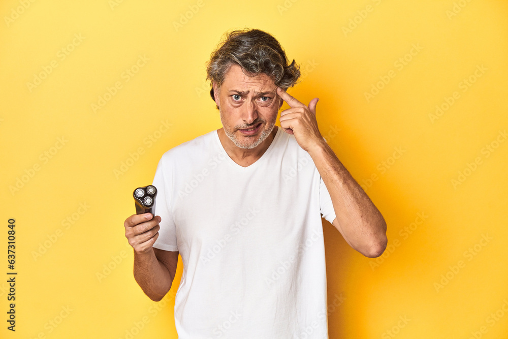 Man holding a razor, yellow studio background showing a disappointment gesture with forefinger. Man holding a razor, yellow studio background showing a disappointment gesture with forefinger.