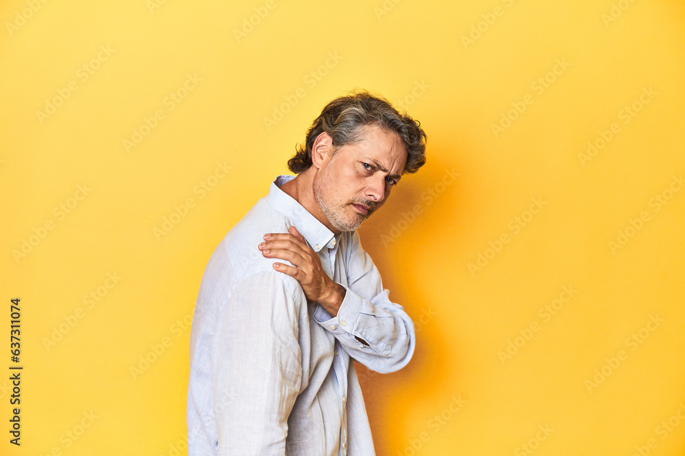 Middle-aged man posing on a yellow backdrop having a shoulder pain. Middle-aged man posing on a yellow backdrop having a shoulder pain.
