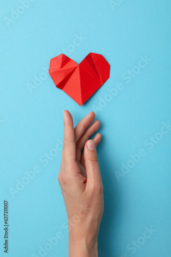 Red paper heart with a hand on a blue background. Blood donation