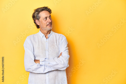 Middle-aged man posing on a yellow backdrop smiling confident with crossed arms.