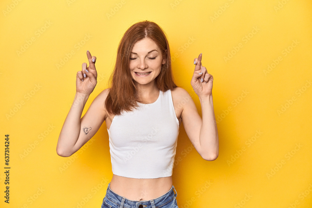 Redhead in white tank top, relaxed studio pose crossing fingers for having luck Redhead in white tank top, relaxed studio pose crossing fingers for having luck