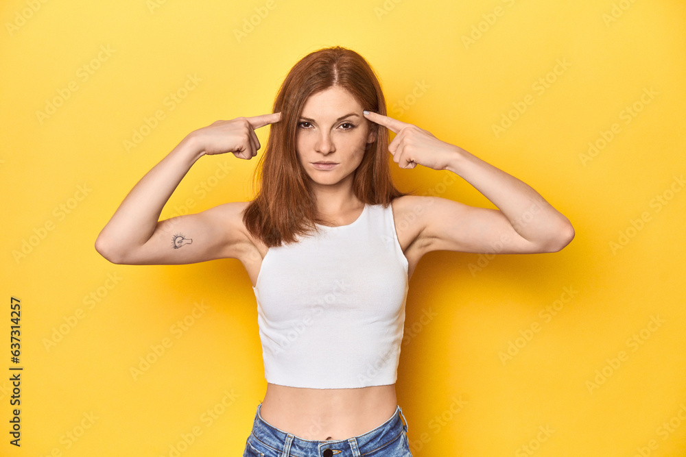 Redhead in white tank top, relaxed studio pose focused on a task, keeping forefingers pointing head. Redhead in white tank top, relaxed studio pose focused on a task, keeping forefingers pointing head.