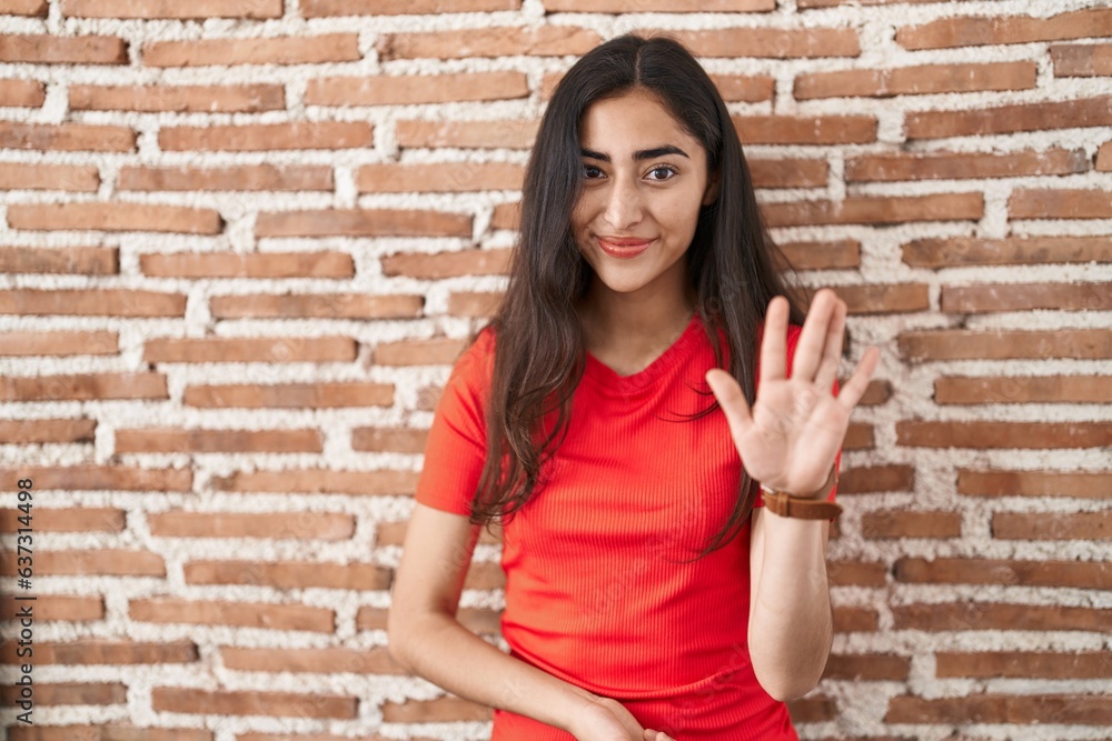 Young teenager girl standing over bricks wall waiving saying hello happy and smiling, friendly welcome gesture Young teenager girl standing over bricks wall waiving saying hello happy and smiling, friendly welcome gesture