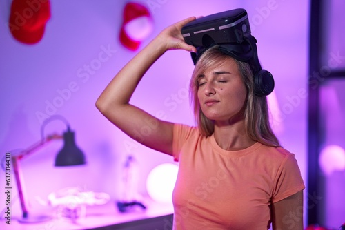 Young blonde woman streamer wearing virtual reality glasses at gaming room