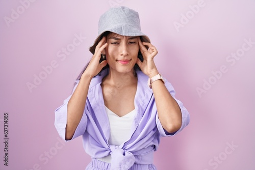 Young hispanic woman standing over pink background wearing hat with hand on head, headache because stress. suffering migraine. © Krakenimages.com