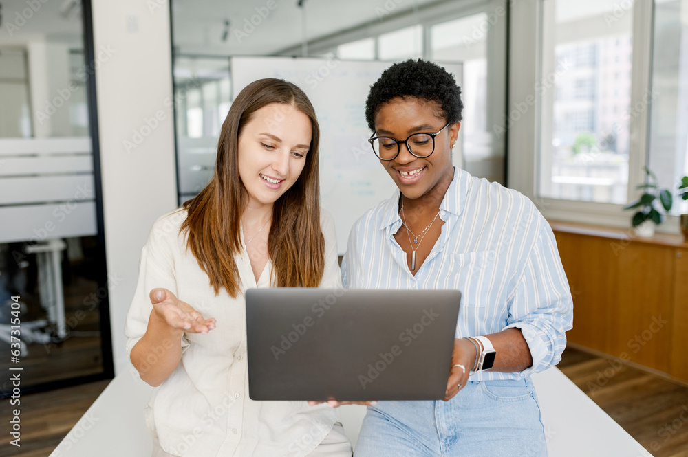 Good cooperation and friendly office atmosphere. Two female colleague discussing project on the laptop. Mentor or coach looking through project of intern, two women with computer in office Good cooperation and friendly office atmosphere. Two female colleague discussing project on the laptop. Mentor or coach looking through project of intern, two women with computer in office