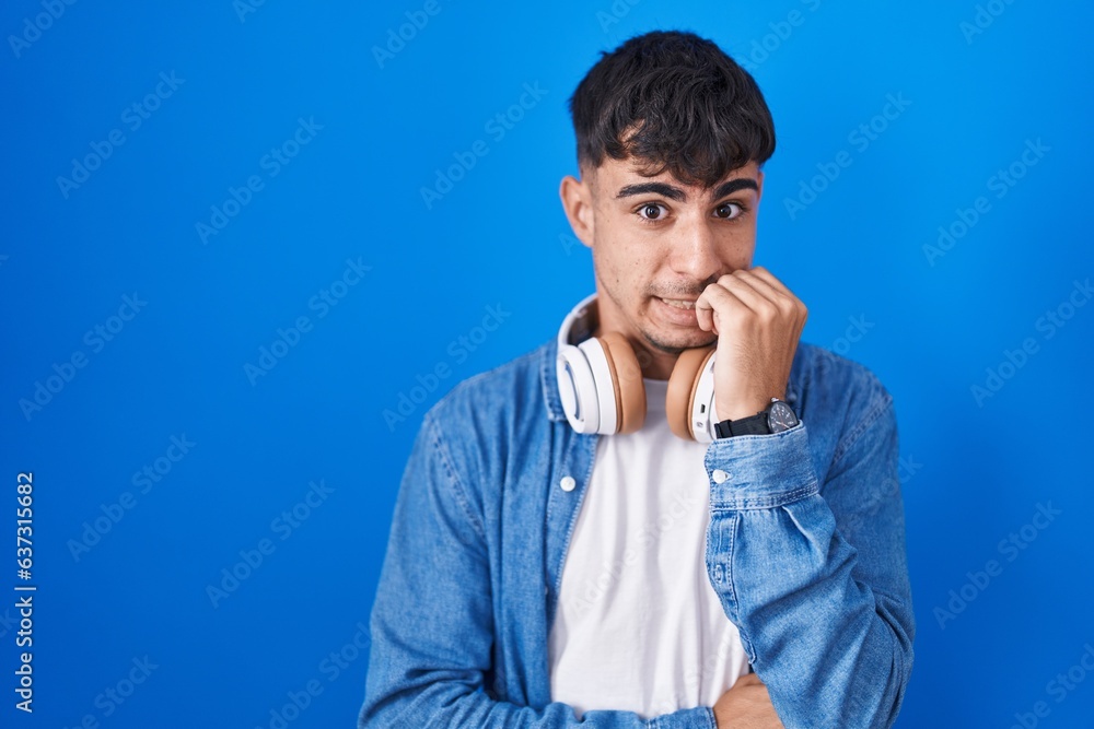 Young hispanic man standing over blue background looking stressed and nervous with hands on mouth biting nails. anxiety problem. Young hispanic man standing over blue background looking stressed and nervous with hands on mouth biting nails. anxiety problem.