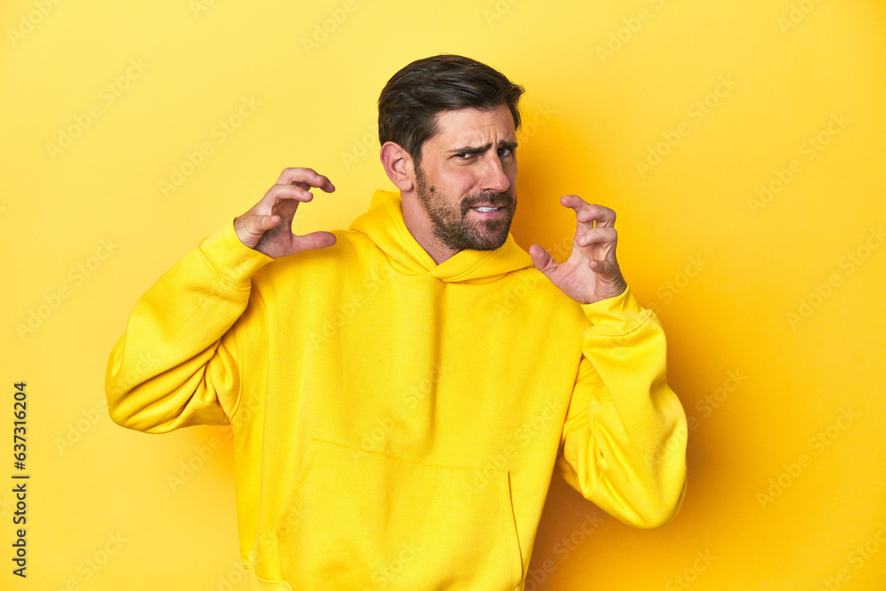Man in yellow hoodie, monochrome studio backdrop screaming with rage. Man in yellow hoodie, monochrome studio backdrop screaming with rage.