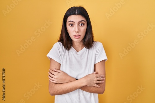 Young beautiful woman standing over yellow background shaking and freezing for winter cold with sad and shock expression on face © Krakenimages.com