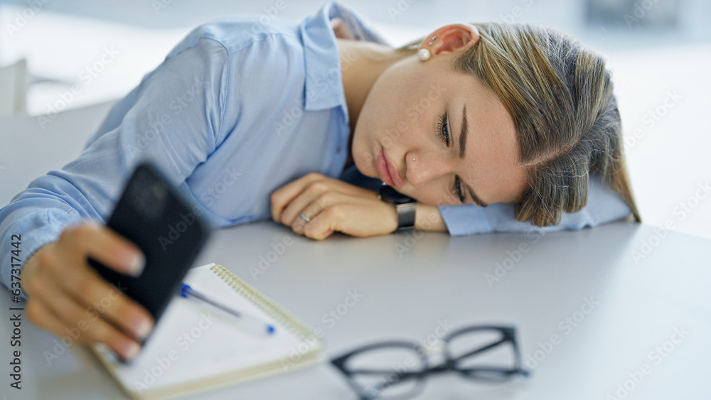 Young blonde woman student using smartphone tired at office Young blonde woman student using smartphone tired at office