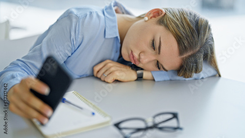Young blonde woman student using smartphone tired at office