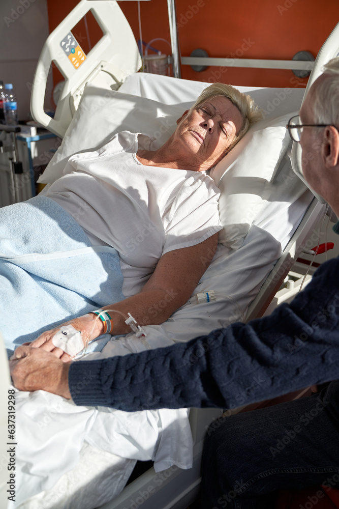 Fototapeta premium Elderly man holding hand of parient lying on bed in hospital
