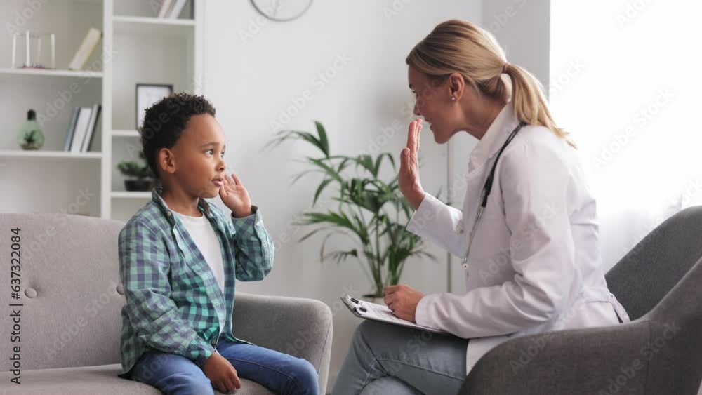 Happy female doctor giving high five to cute little African American boy patient at hospital consultation. A smiling pediatrician will cheer up a small child at the clinic. Healthcare concept. Happy female doctor giving high five to cute little African American boy patient at hospital consultation. A smiling pediatrician will cheer up a small child at the clinic. Healthcare concept.