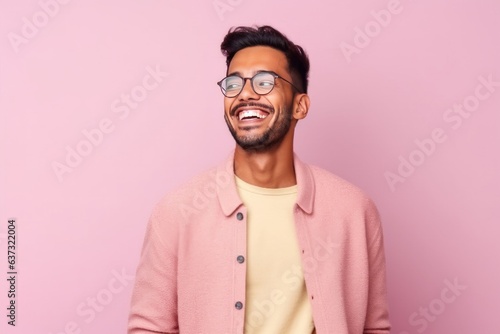 Portrait of young indian man in eyeglasses laughing against pink background © Anne-Marie Albrecht