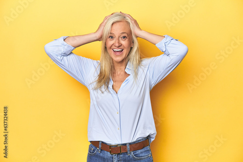 Middle-aged Caucasian woman in blue shirt, yellow studio screaming, very excited, passionate, satisfied with something.
