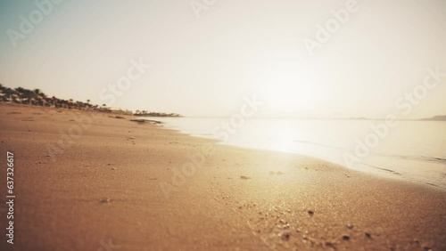 Camera moving over sandy ocean beach at sunset on luxury resort with palm trees, umbrellas, sunbeds on shore. Calm water surface and footprints on sand. Travel, tourism, journey, destination concept. photo