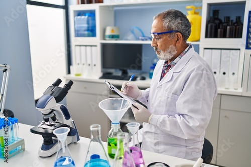 Senior grey-haired man scientist writing report working at laboratory